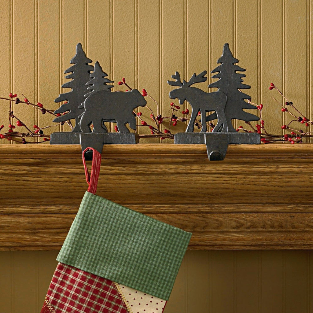 Christmas stocking holders hanging on a mantel with decorative metal animals above.