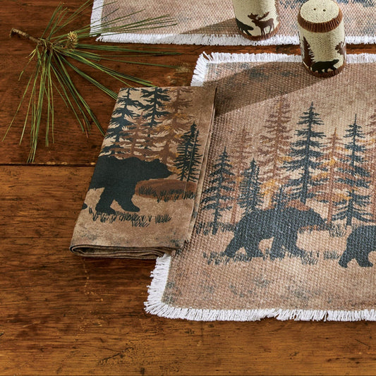 Table setting with bear and forest design placemats and plates on a wooden table.