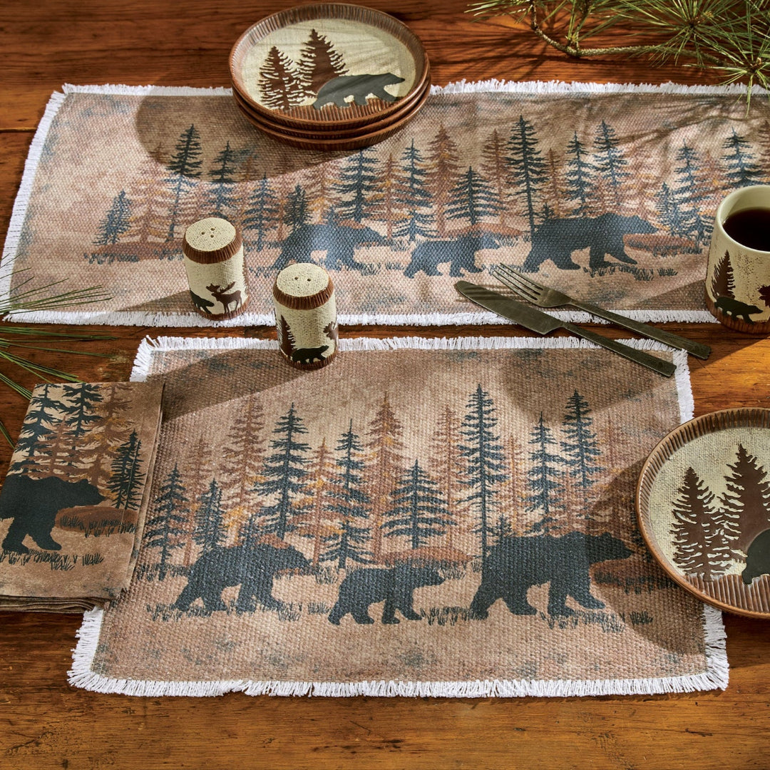 Table setting with bear and forest design placemats and plates on a wooden table.