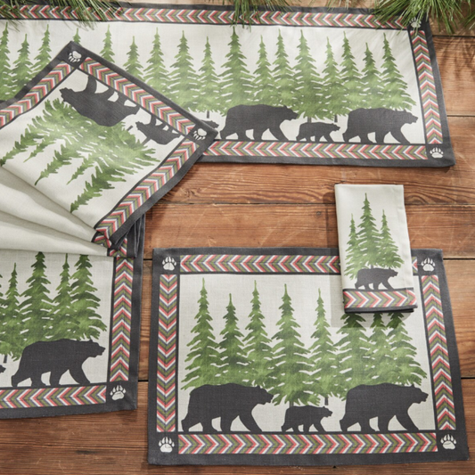 Set of placemats and napkins and table runner with bear and forest design on a wooden surface