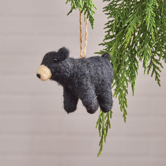 Felted bear ornament hanging from a branch with a plain background