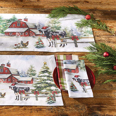 Set of Christmas-themed table linens with a barn and farm scene on a wooden table.