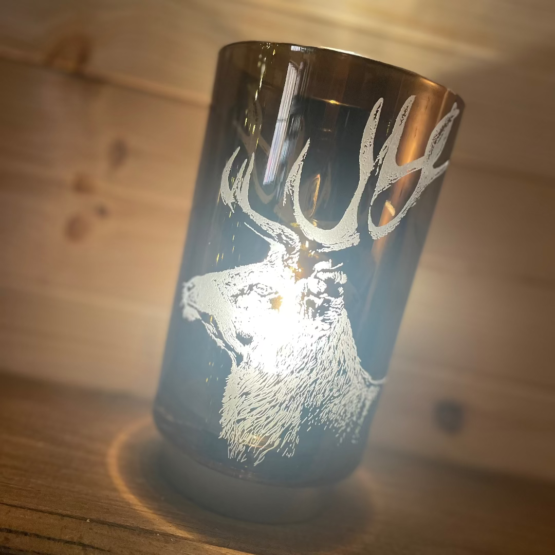 Glass battery operated lamp with deer design on a wooden surface
