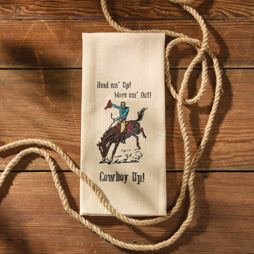 Cotton tea towel with cowboy graphic and text on a wooden surface with rope