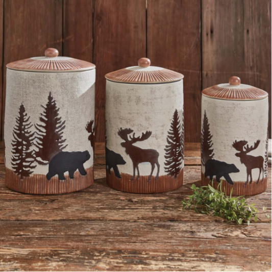 Three decorative canisters with animal and tree designs on a wooden surface.
