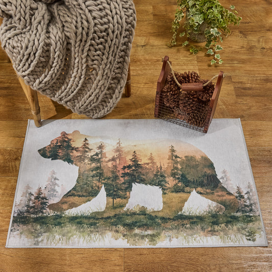 A rectangular area rug with a bear silhouette filled with a forest scene, styled on a wooden floor with a chunky knit blanket, a basket of pinecones, and a potted plant nearby.