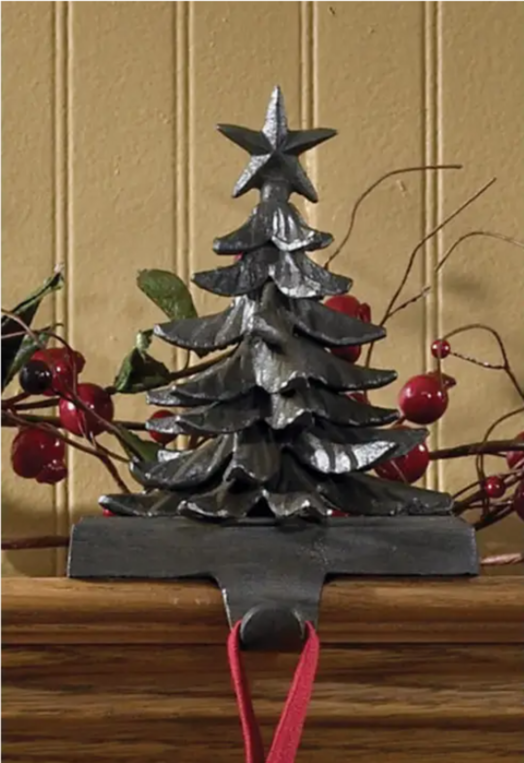 Decorative iron Christmas tree Stocking Holder with a star on top, hanging on a wooden surface.