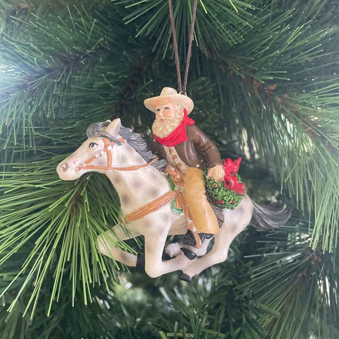 Ornament of a cowboy on a horse hanging on a Christmas tree.