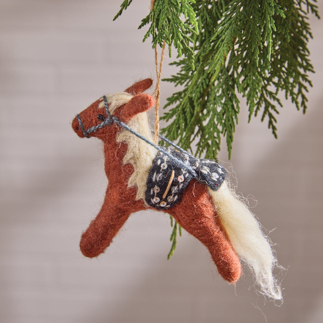 Felt horse ornament with a bridle hanging from a tree branch.