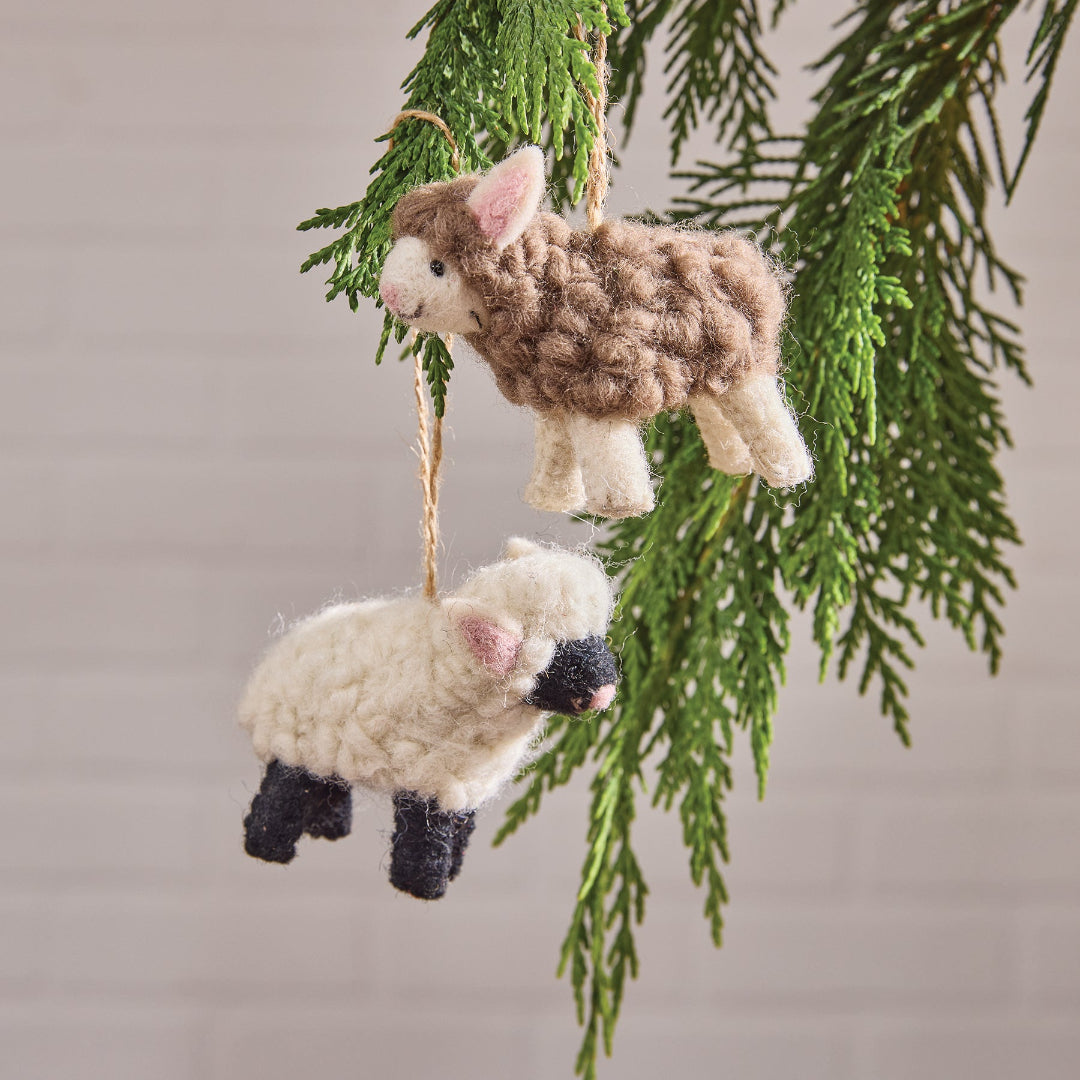 Two Wool felt sheep ornaments hanging from a branch against a neutral background