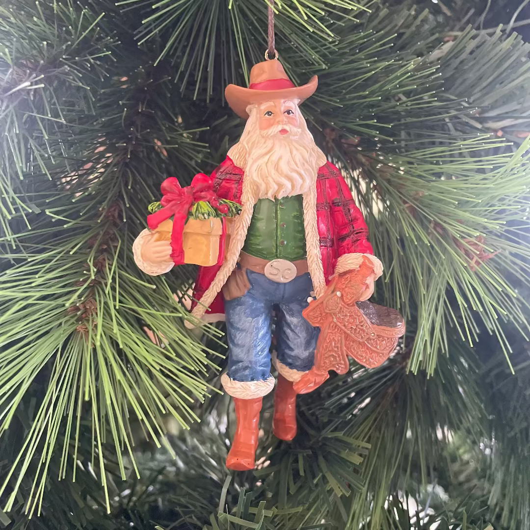 Christmas ornament of a Santa in a red coat and cowboy hat hanging on a tree.