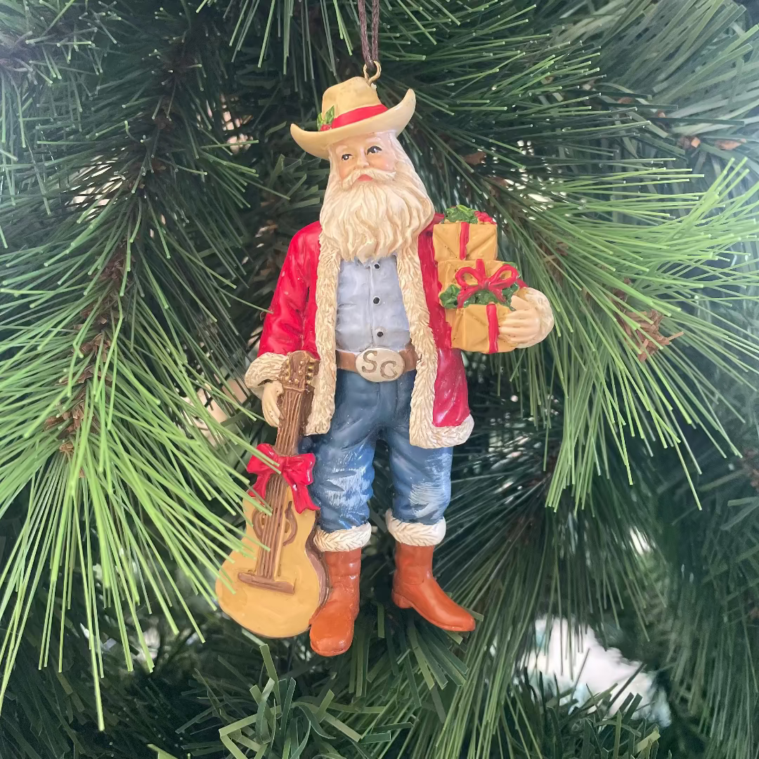 Christmas ornament of a cowboy Santa with a guitar and gift on a tree.