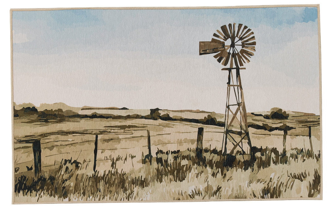A watercolour landscape rug featuring a rustic metal windmill in a grassy field, with a fence line and distant hills under a pale blue sky.